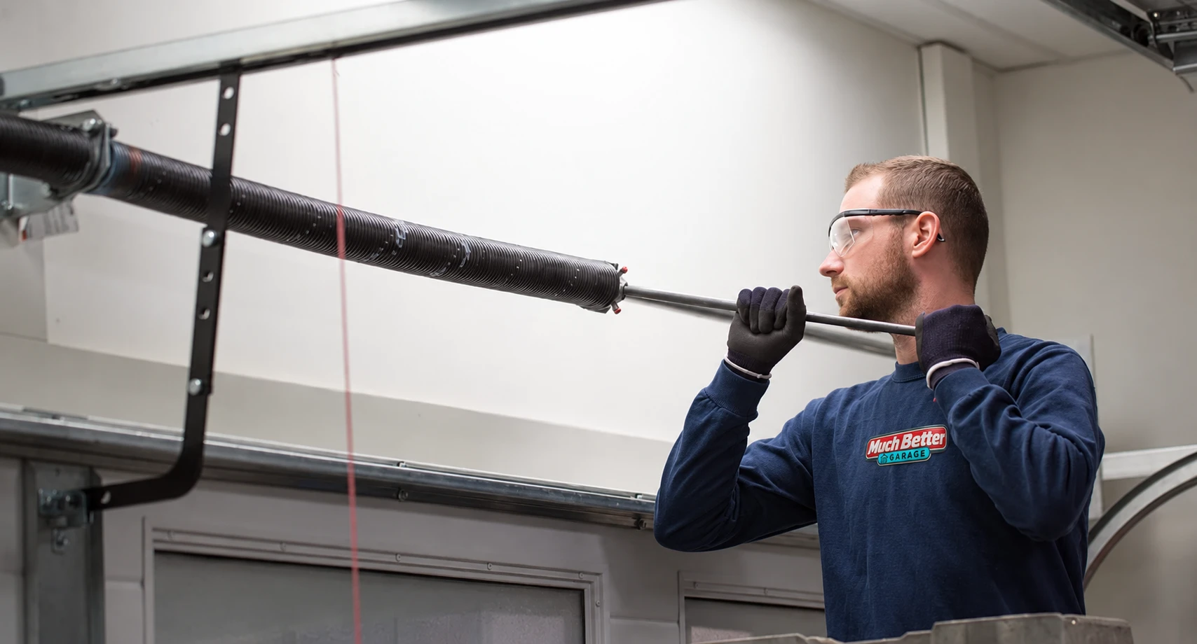 Technician wearing a Much Better Garage uniform working on a garage door spring